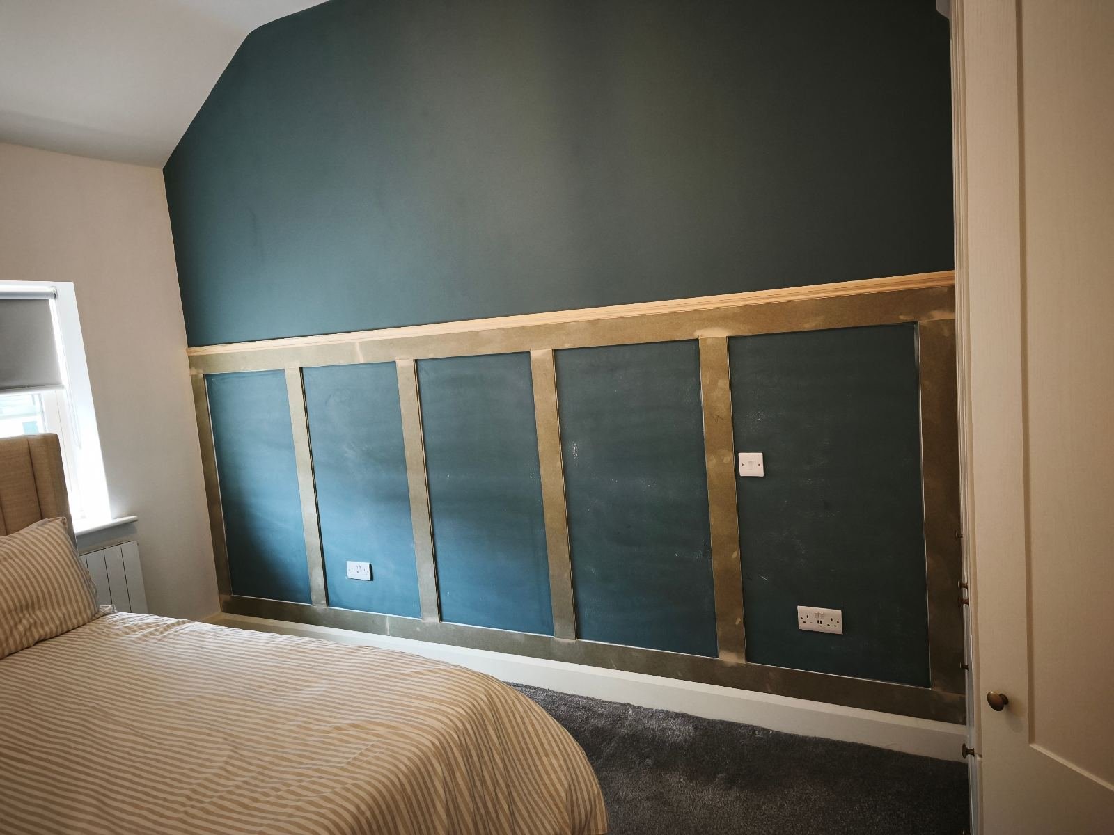 Shaker panelling fitted behind a bed in a Dublin bedroom, dark teal wall with squares set out around the sockets